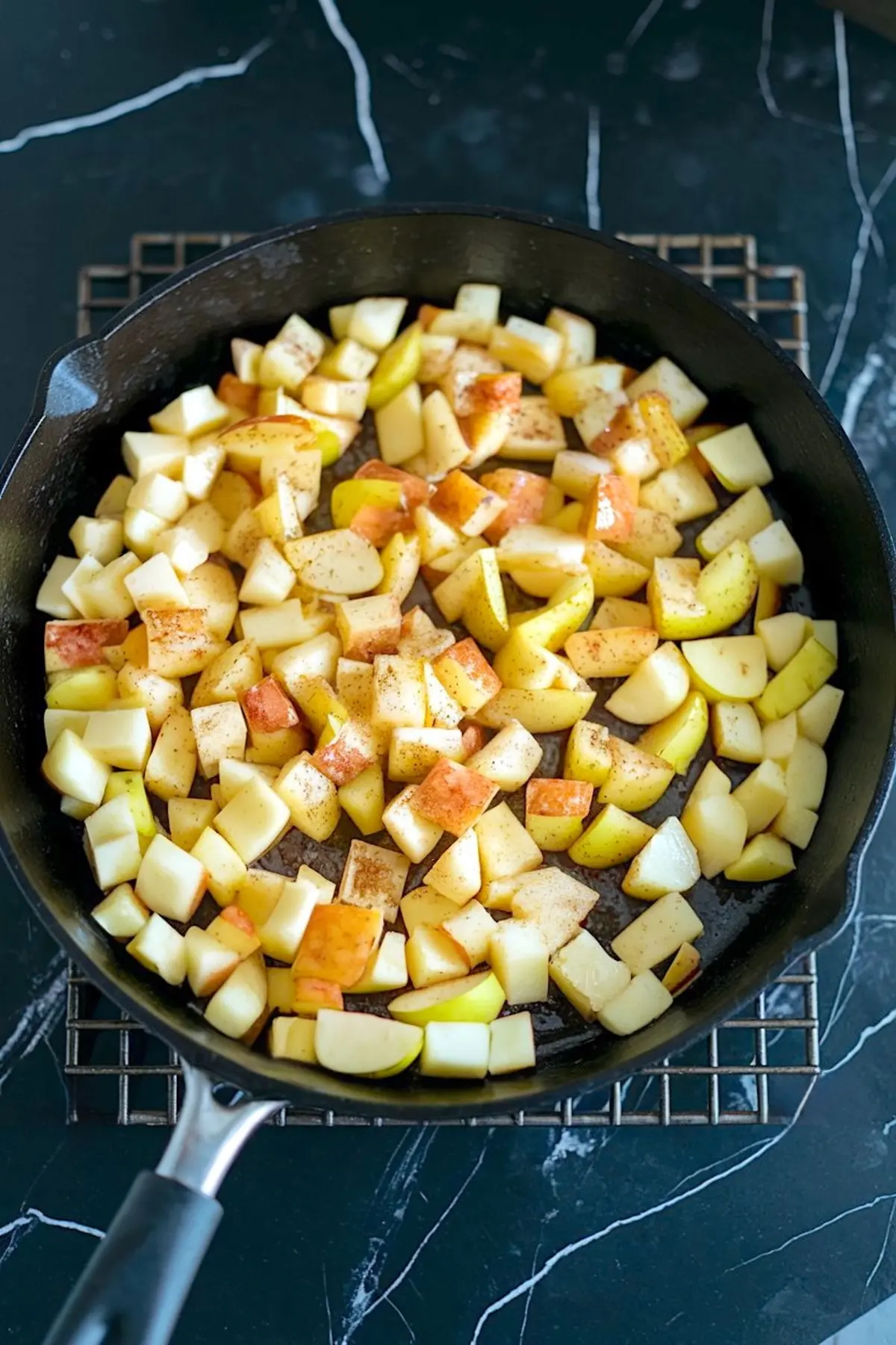 Top view of a black cast iron skillet filled with diced apples sprinkled with cinnamon and sugar, prepared for caramel apple topping.