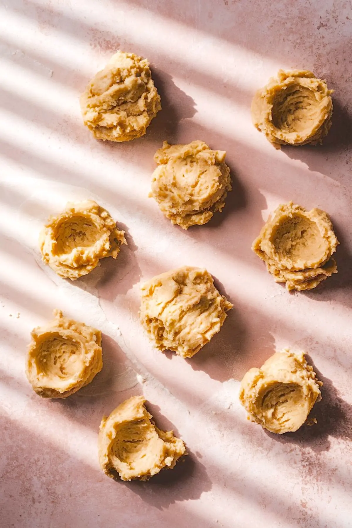 Unbaked biscuit dough portions arranged on parchment paper, showing the textured, scooped dough ready for baking with visible indentations.