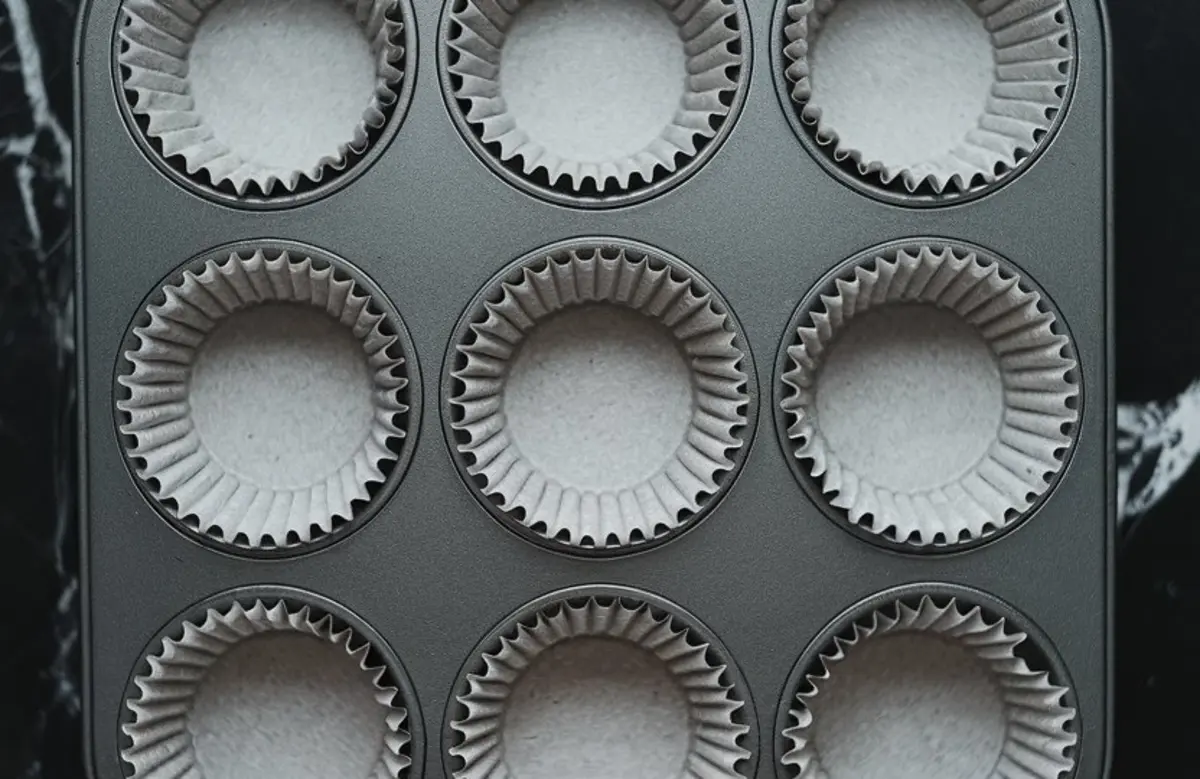 Metal cupcake tray lined with plain white paper liners, ready for filling with muffin or cupcake batter.