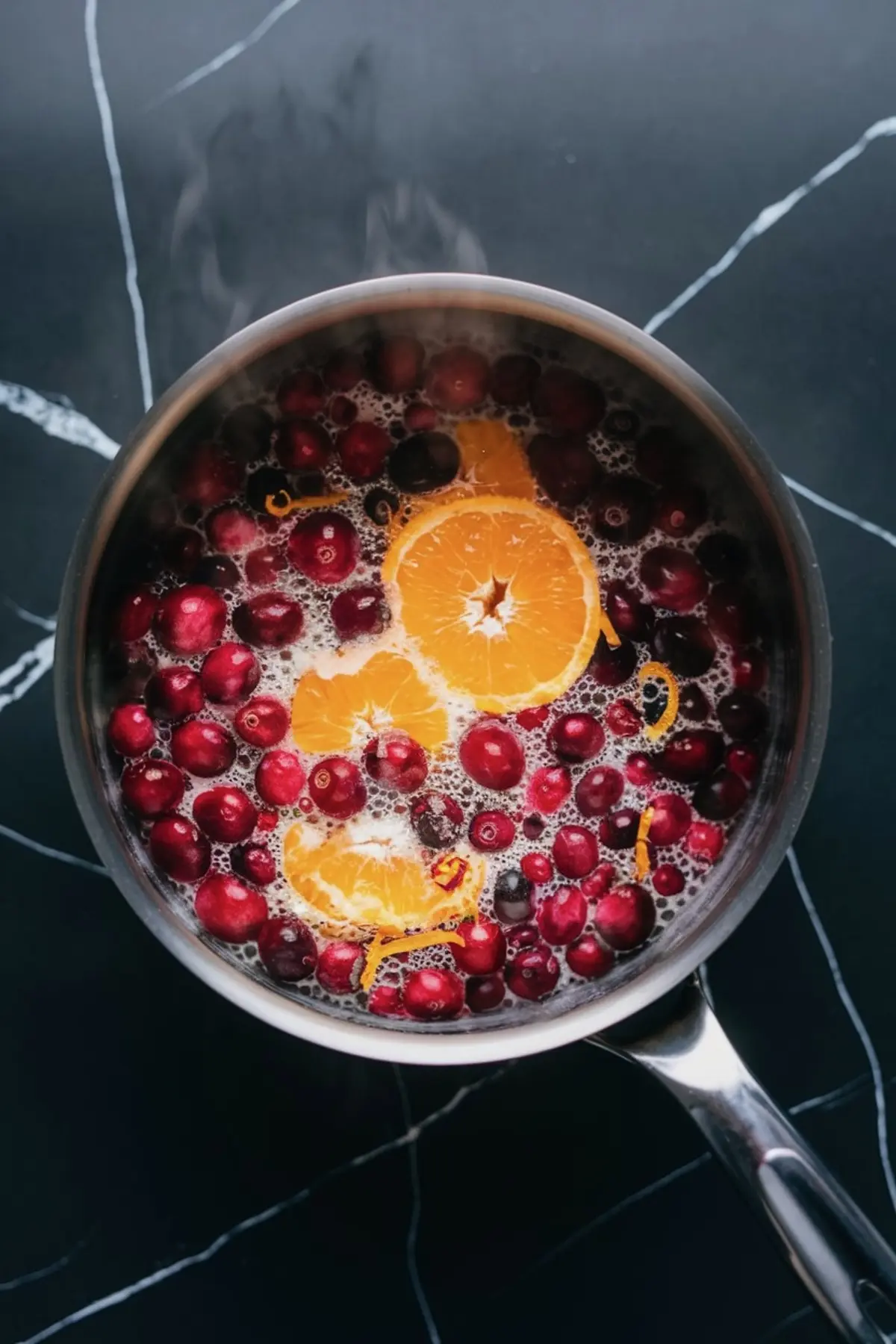 Simmering cranberry sauce in a saucepan with fresh cranberries, orange slices, and zest, capturing holiday flavor for orange cranberry cheesecake and cranberry cake recipes.