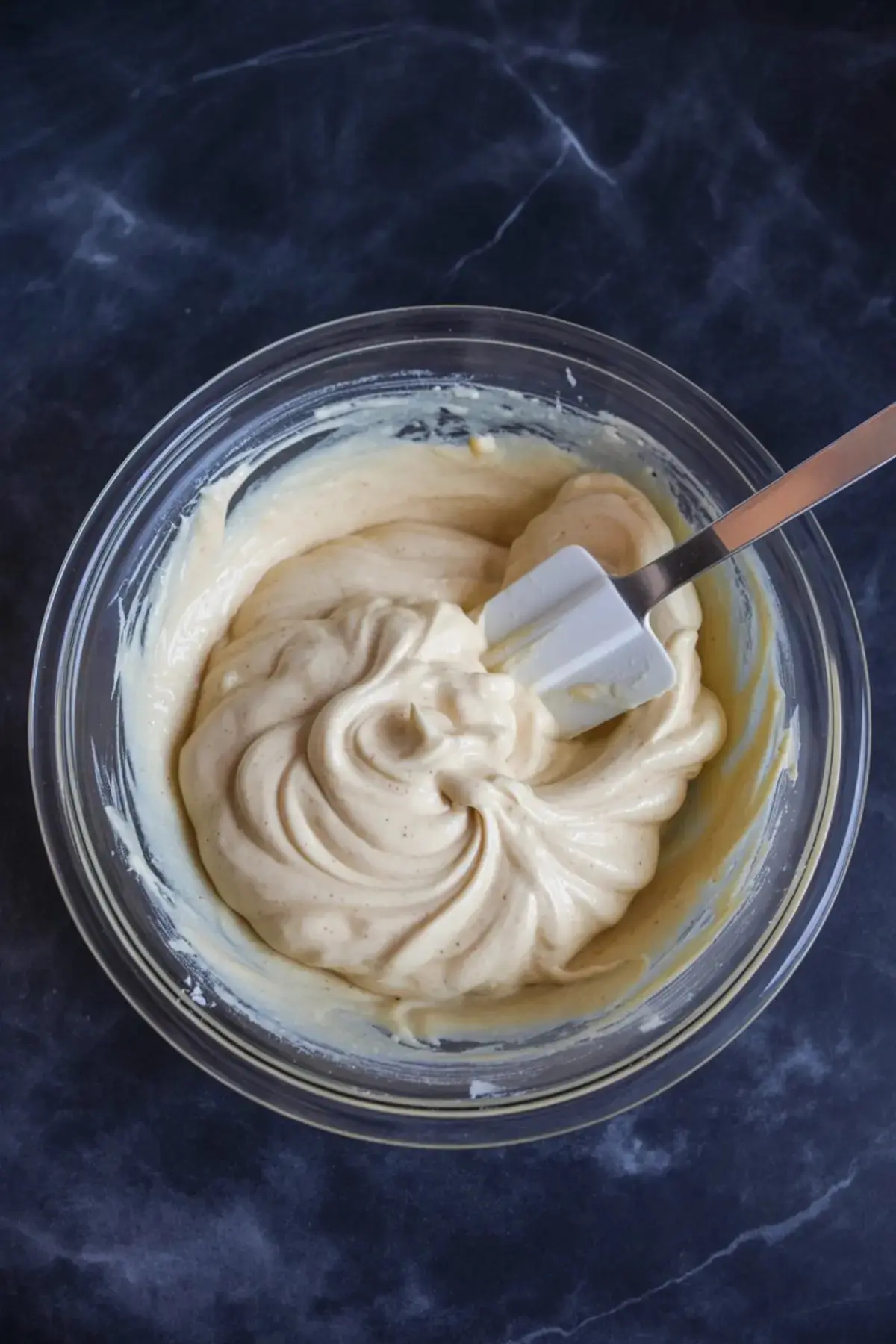 Creamy cheesecake batter swirled in a mixing bowl with a spatula, ready to be poured into a crust—essential for cranberry orange cheesecake and white chocolate cranberry cheesecake.