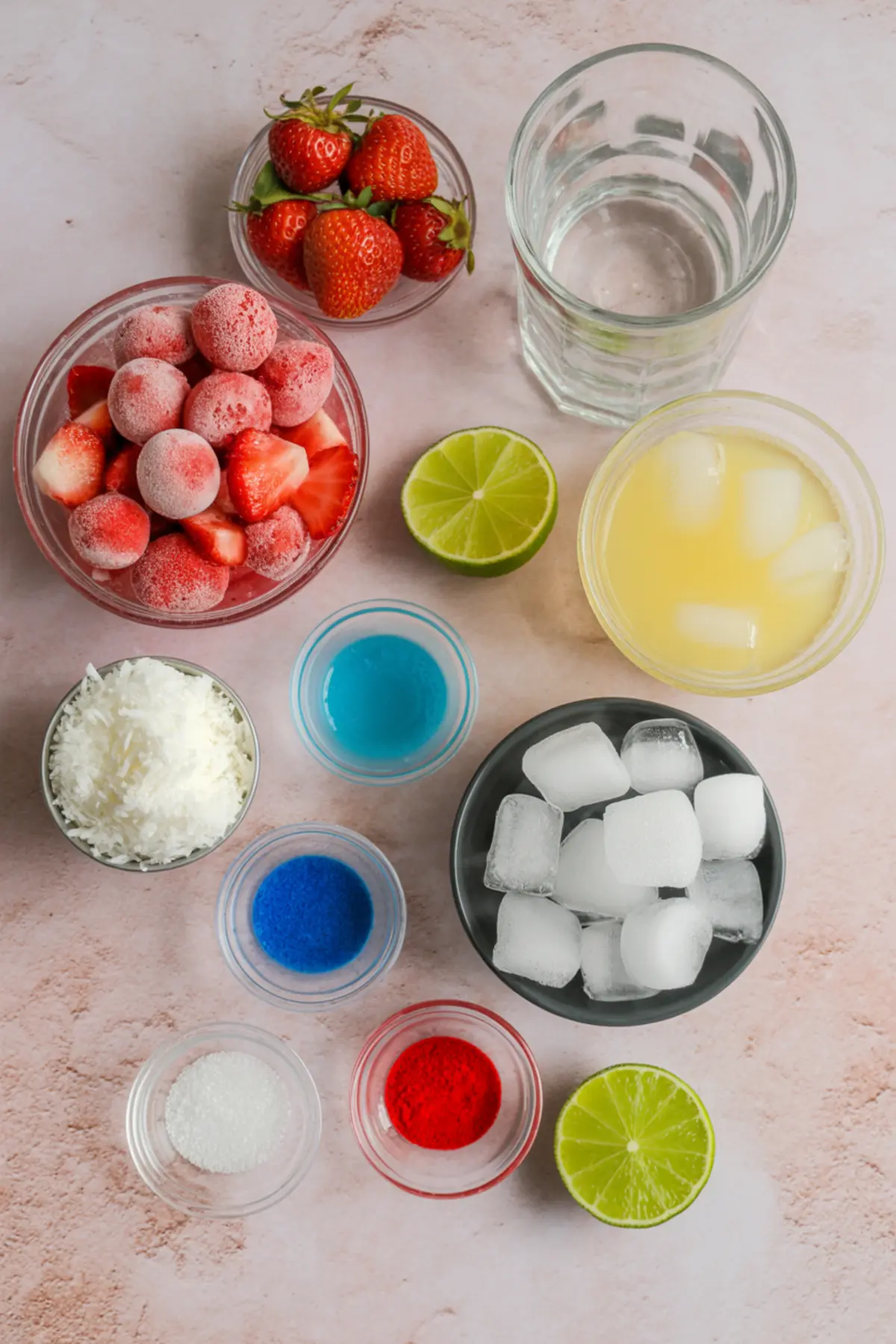 Flat lay of margarita ingredients including frozen strawberries, fresh strawberries, coconut, blue curaçao, lime juice, simple syrup, food coloring, and ice on a pink background.
