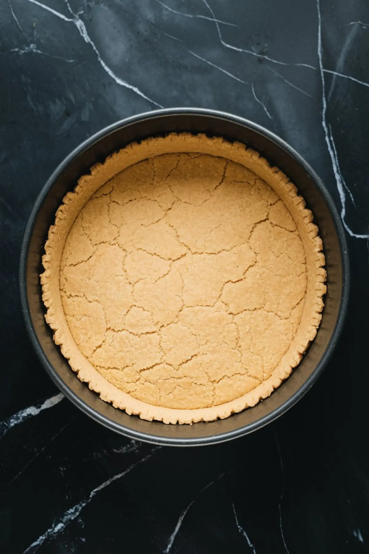 Overhead image of a baked cookie crust for cheesecake inside a round pan, with a golden, slightly cracked surface.