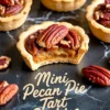 Close-up shot of a mini pecan tart cookie with a bite taken out, revealing the sticky pecan pie filling. The flaky tart shell and glossy pecan topping sit on a dark marble background, surrounded by additional mini tarts and loose pecan halves.
