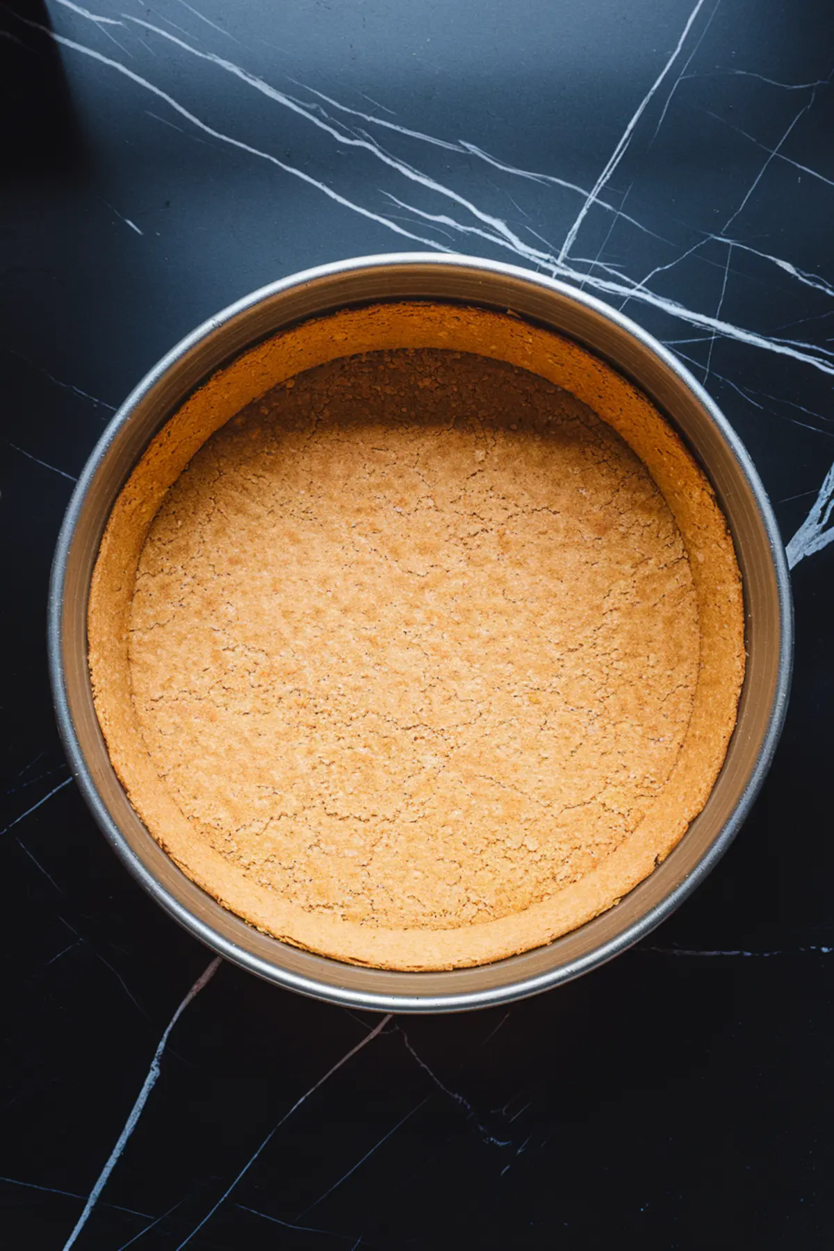 Round springform pan with a smooth, golden-baked graham cracker crust pressed into the base and sides, ready for filling.