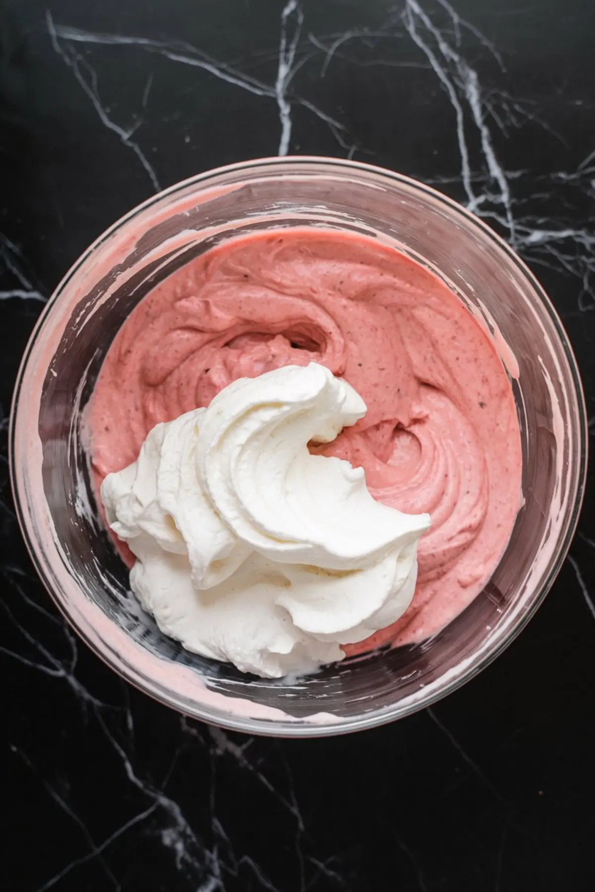 Mixing bowl with fresh strawberry cream filling partially blended with a dollop of fluffy whipped cream, highlighting the light and airy texture preparation.