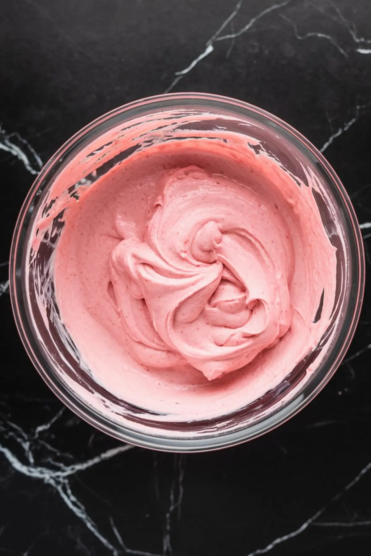Fully mixed pink strawberry cheesecake filling in a glass bowl, with a soft, velvety consistency ready to be spread into a crust.