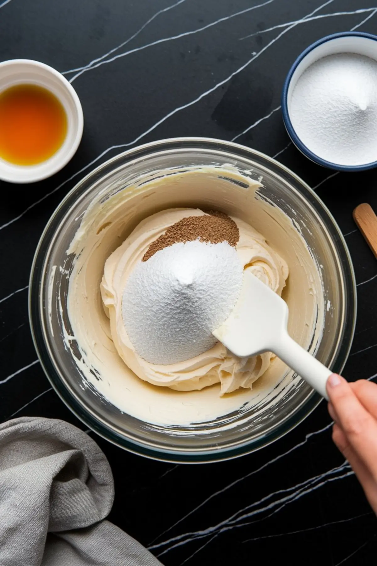 Mixing Oreo cheesecake filling with powdered sugar and vanilla extract in a glass bowl for a creamy no bake Oreo cheesecake.