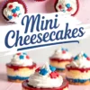 Mini cheesecakes with red fruit topping, creamy white filling, and blue crusts, garnished with piped whipped cream and red, white, and blue star sprinkles.