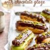 Tray of chocolate-dipped pistachio éclairs with green pistachio filling and chopped nuts, arranged on parchment paper for dessert presentation.