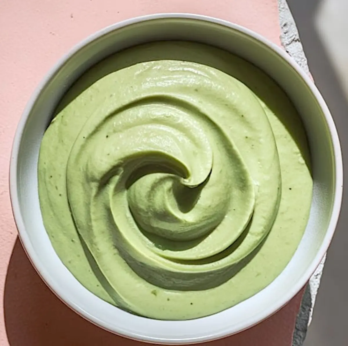 Close-up of smooth pistachio cream swirled in a white bowl, showcasing a rich and creamy green texture for pastry filling.