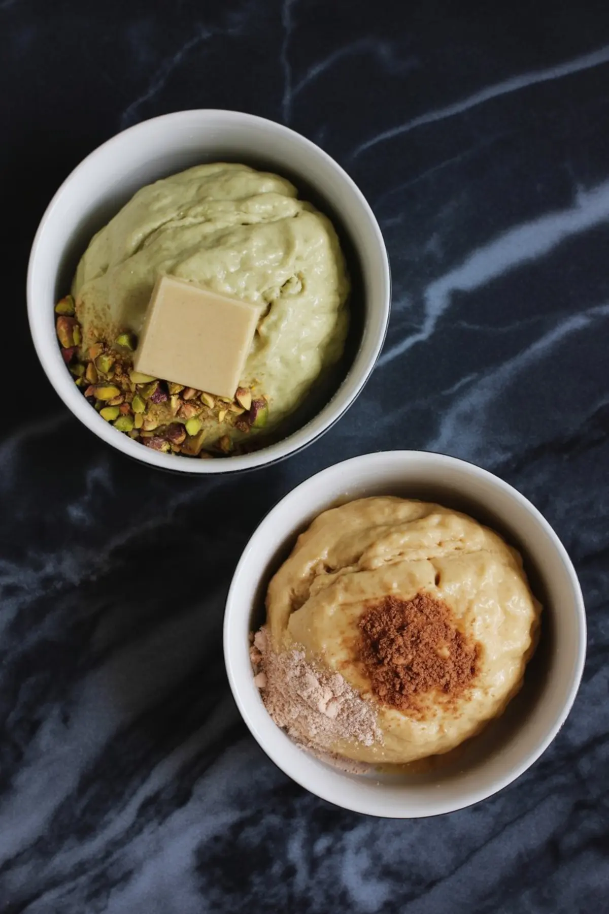 Two bowls of prepared cookie dough mixtures, one with pistachios and white chocolate, the other with brown sugar, ready for baking pistachio pudding sandwich cookies.