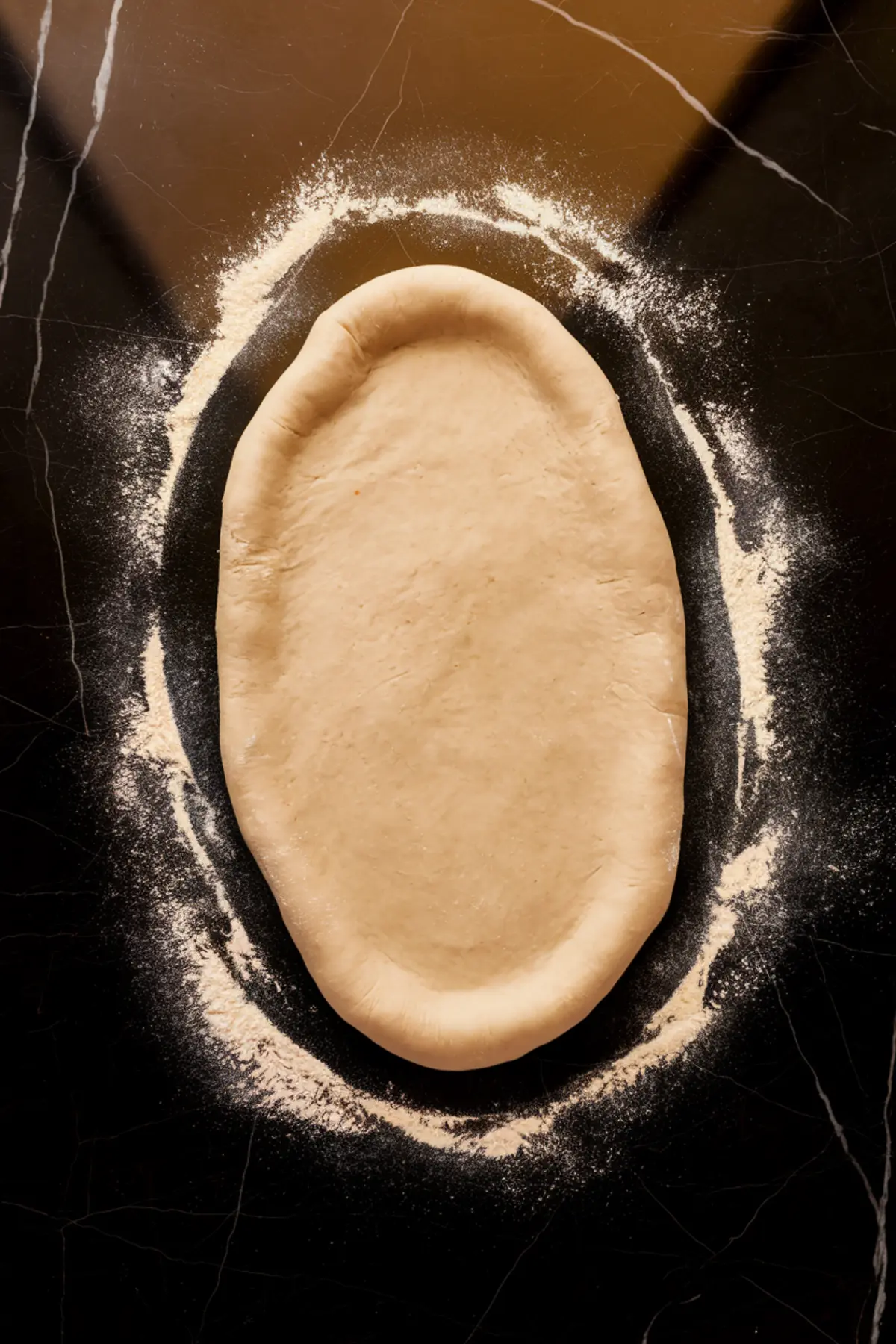 An overhead shot of an oval-shaped raw shortbread dough resting on a black marble surface, lightly floured and ready for baking.