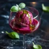 Single glass of plum sorbet with basil oil drizzle and basil garnish, highlighted with the text “Plum Sorbet with Basil Oil Drizzle” on a moody background.