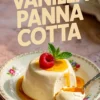 Silky vanilla panna cotta topped with a raspberry and mint, draped in caramel sauce, on a decorative porcelain plate with a spoonful taken out.