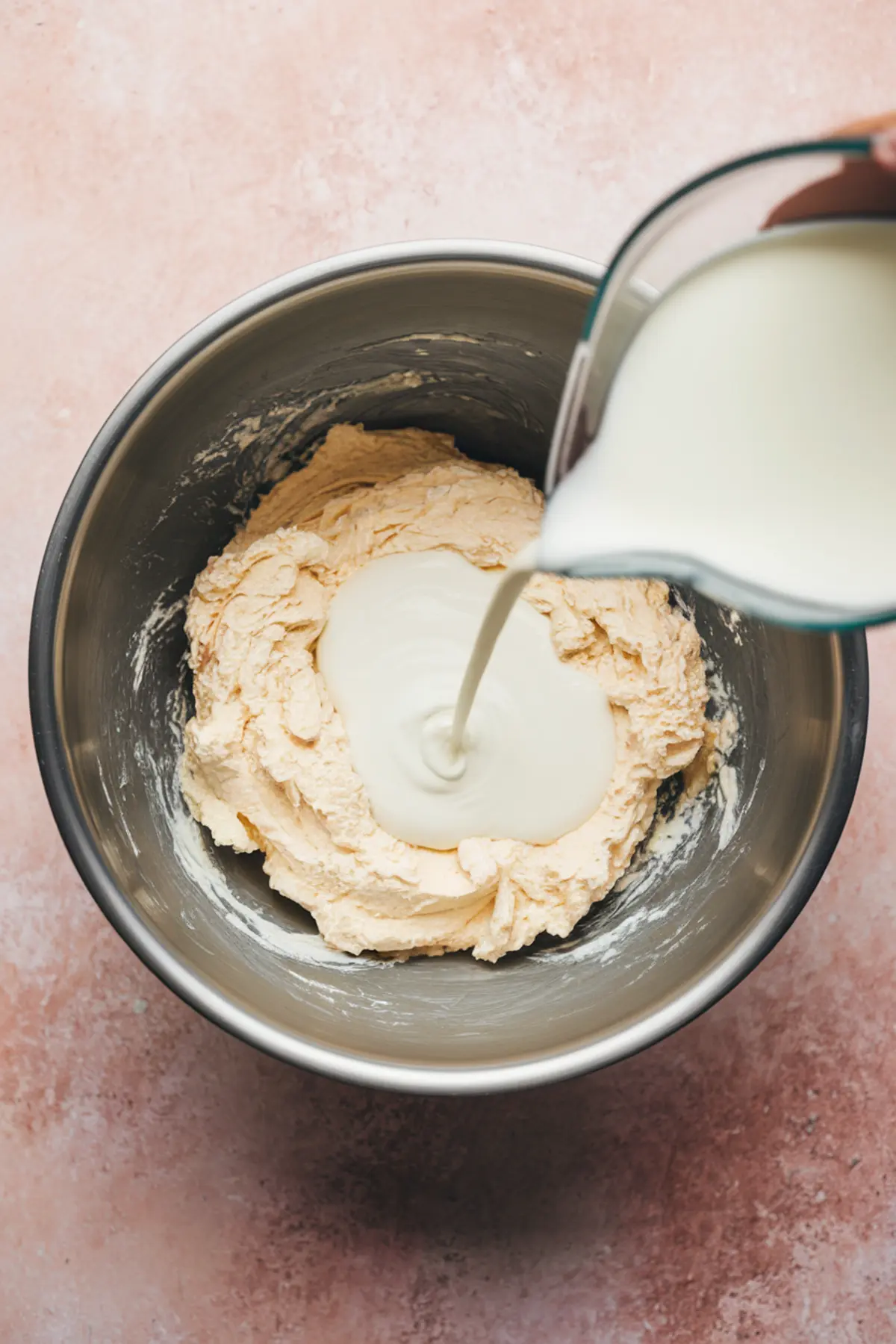Mixing bowl with thick cream cheese mixture and milk being poured in, capturing the process of making a smooth dessert dip base for apple slices or fruit platters.