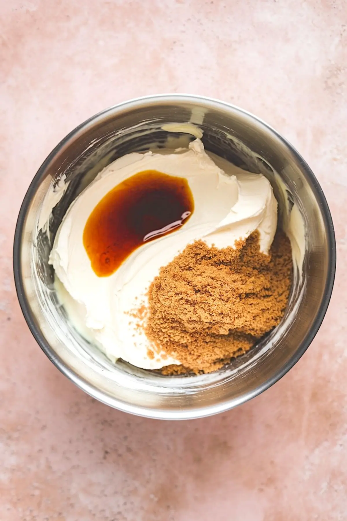 Stainless steel mixing bowl containing cream cheese, brown sugar, and vanilla extract, highlighting ingredients for a sweet and creamy apple dip.