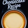 Freshly baked cheesecake with golden brown edges and smooth top displayed with text “Baked Cheesecake Recipe” on black background, showcasing how to make a cheesecake.