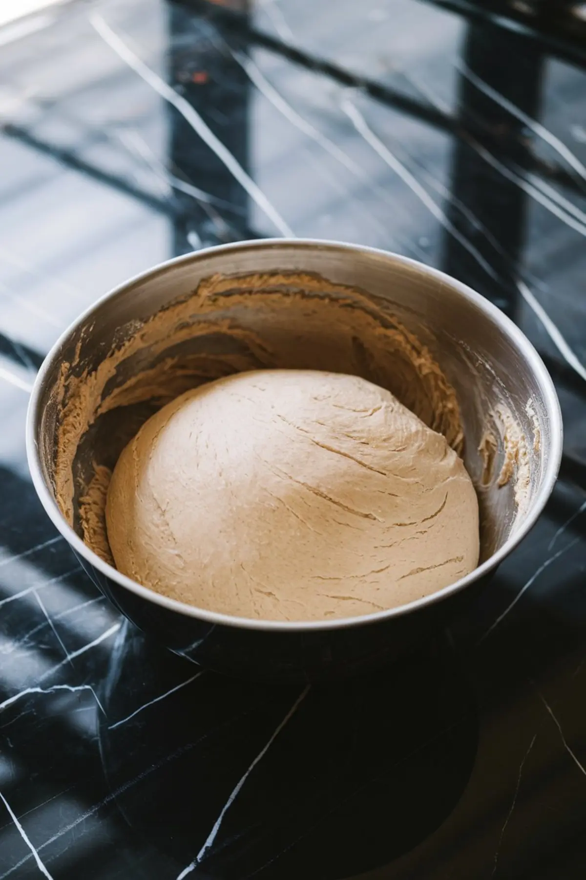 Round cookie dough resting in a mixing bowl on a black marble counter after being prepared and kneaded for baking.