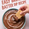 Hand dipping a rectangular graham cracker into a bowl of rich, glossy brownie batter dip with text overlay that reads “Easy Brownie Batter Dip Recipe.”