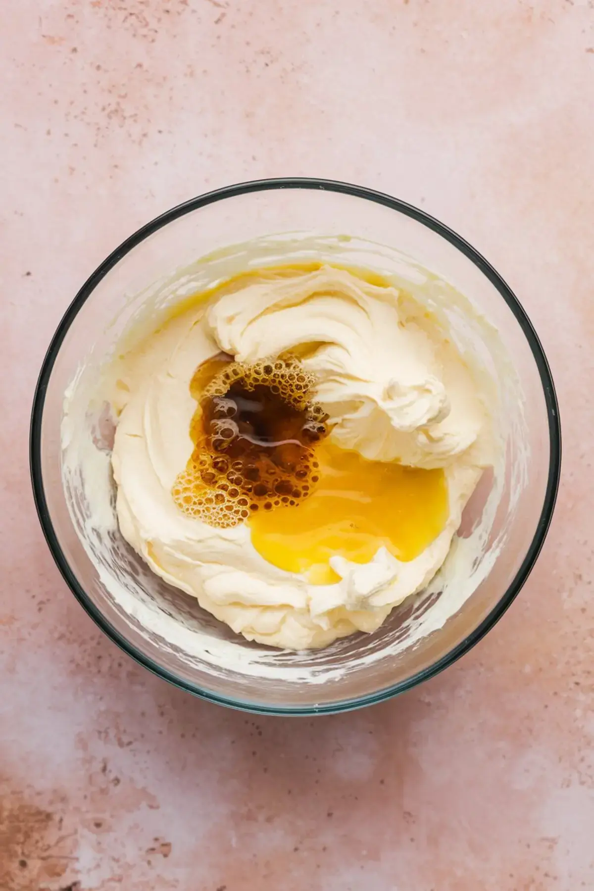 Cream cheese mixture with added egg and vanilla extract in a mixing bowl, highlighting the ingredients before blending for cheesecake dip preparation.