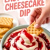Close-up of easy cherry cheesecake dip in a teal bowl, showing thick swirls of creamy cheesecake filling layered with vibrant cherry sauce and whole cherries, with a hand dipping a graham cracker.