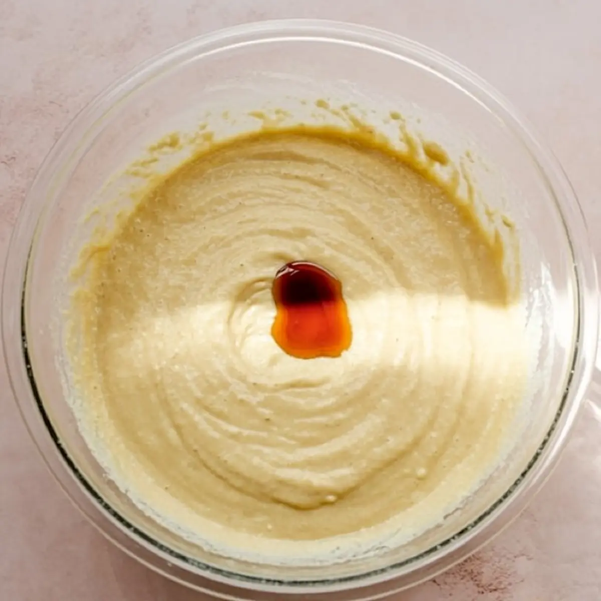 Smooth batter in a glass bowl with a splash of vanilla extract in the center, ready to be blended into chocolate chip dip.