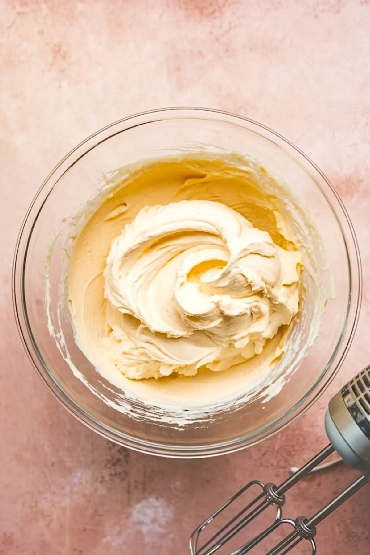 Thick whipped mixture of butter and cream cheese in a glass bowl, swirled smoothly and ready for sweet dip preparation.