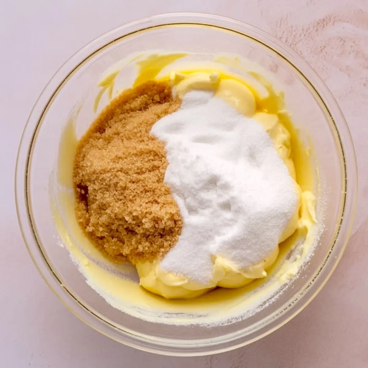 Bowl of butter, brown sugar, and granulated sugar before mixing, with a creamy yellow base and distinct sugar layers.