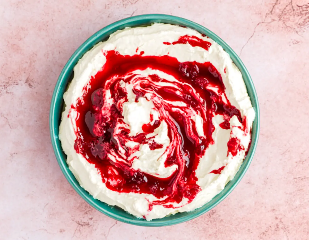 Top-down view of cranberry cream cheese dip in a turquoise bowl, featuring a vibrant red cranberry swirl over a fluffy white cream cheese base.