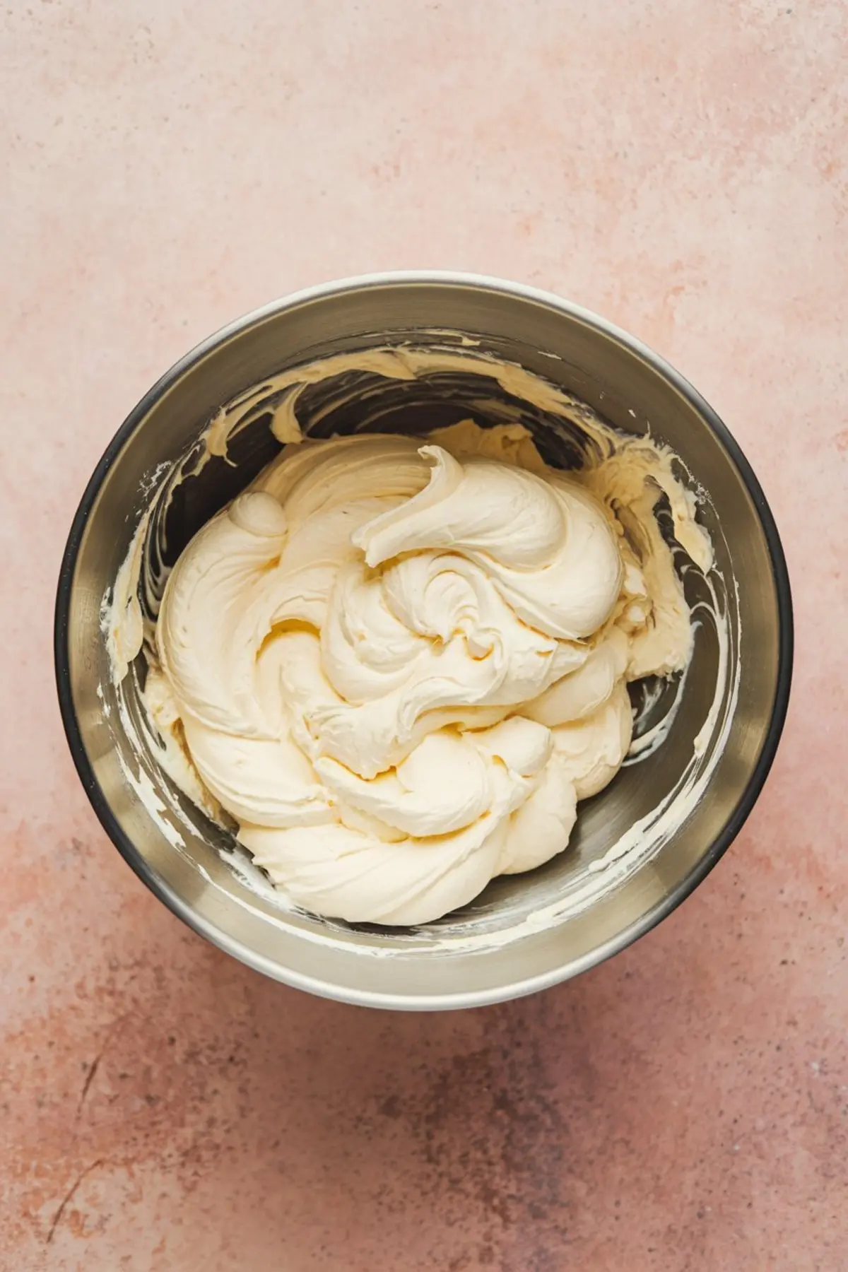 Smooth and fluffy whipped cream cheese mixture in a metal mixing bowl, showing soft peaks and light texture.