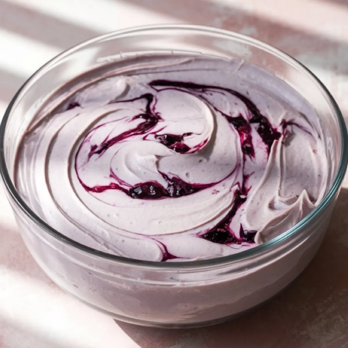 Glass bowl filled with purple blueberry cream mixture swirled with dark blueberry compote, ready for pie assembly or freezing.