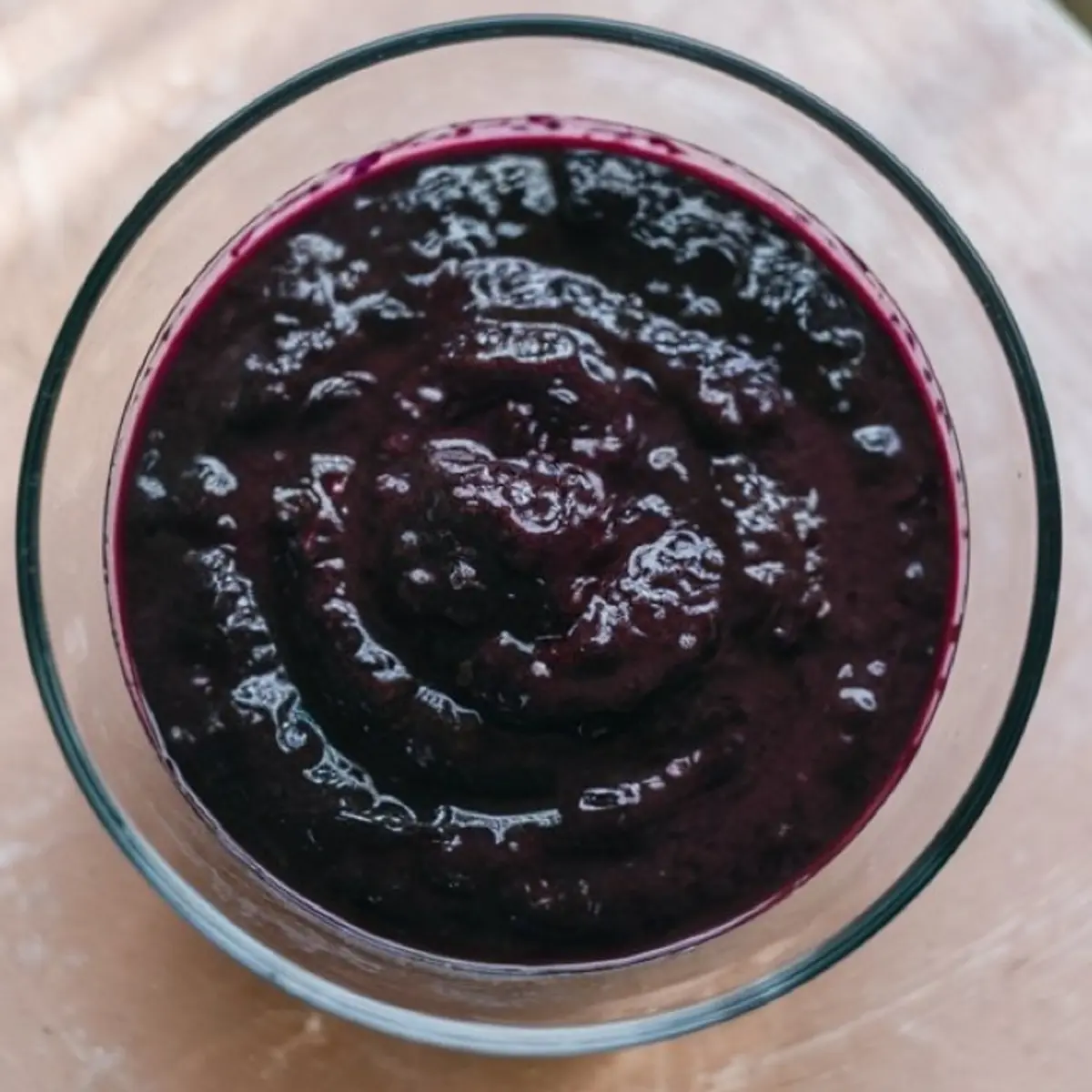 Glass bowl filled with thick, dark purple blueberry compote or puree, showing a rich texture and glossy surface.