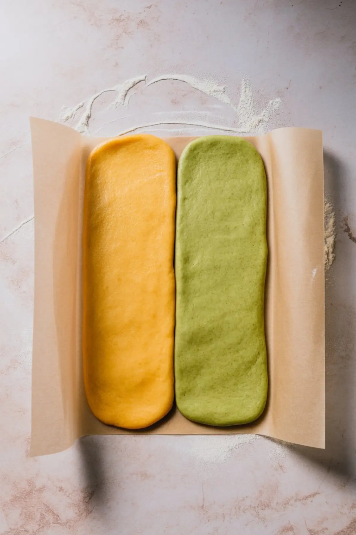 Rectangular mango and matcha cookie doughs side by side on parchment paper, pressed flat and chilled, ready to form swirl cookies.