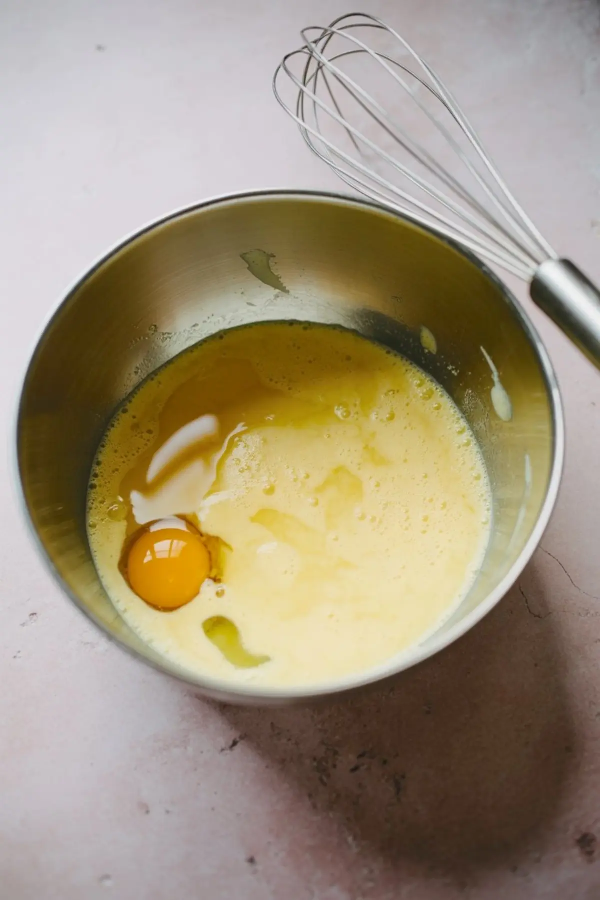 Overhead view of baking ingredients for matcha strawberry cake, including flour, matcha powder, sugar, eggs, strawberries, strawberry puree, ricotta, cream cheese, oil, milk, and vanilla extract arranged on a pink surface.
