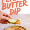 Hand holding a green apple slice dipped into creamy peanut butter dip, with a bowl of smooth peanut butter spread below and bold orange text reading “Peanut Butter Dip.”