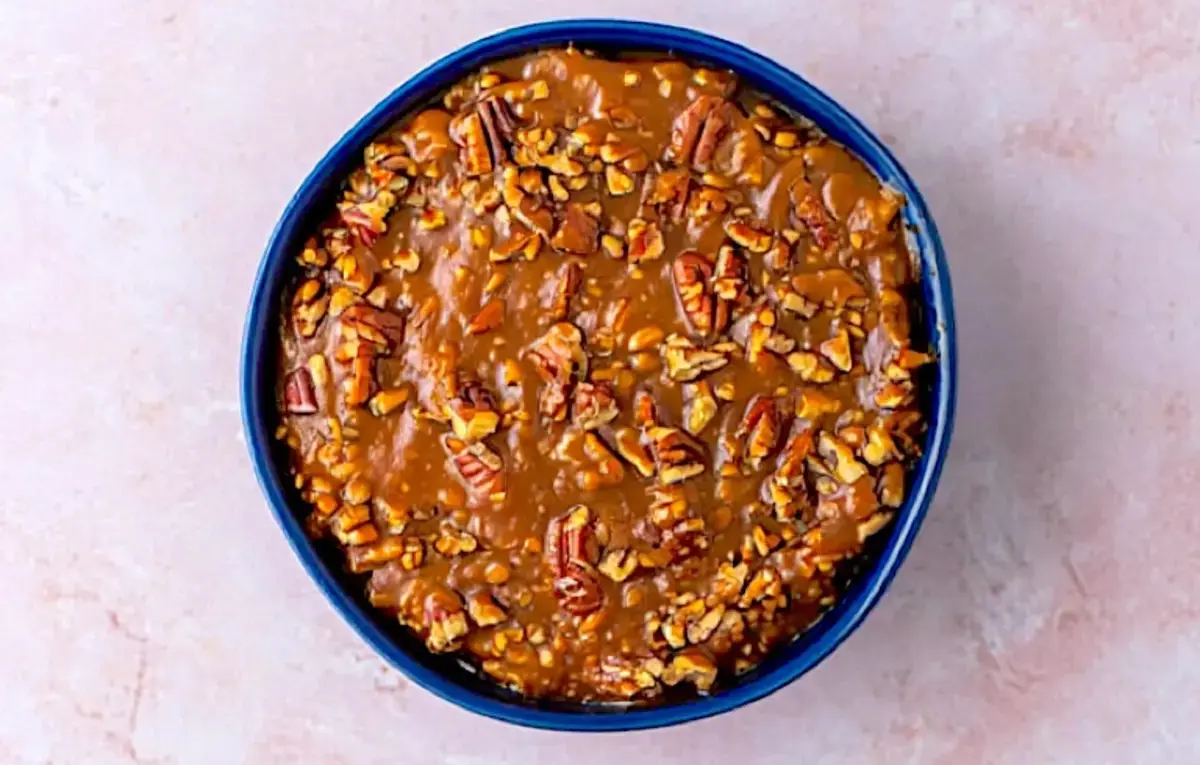 Thick pecan pie dip set in a blue ceramic bowl, topped with chopped and halved pecans, showing the finished dessert ready to cool or serve.
