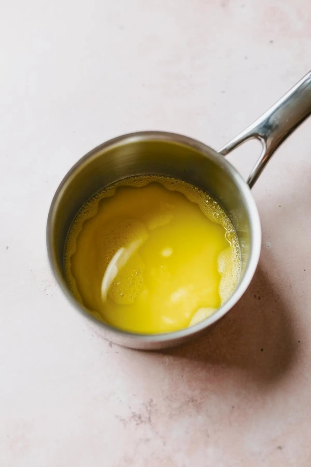 Small saucepan filled with freshly melted butter on a pink counter, part of the preparation steps for a pecan pie dip recipe.
