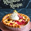 Baked rhubarb pie with a golden lattice crust and a dollop of whipped cream on top, served on a pink plate with text overlay reading "Rhubarb Pie Recipe."