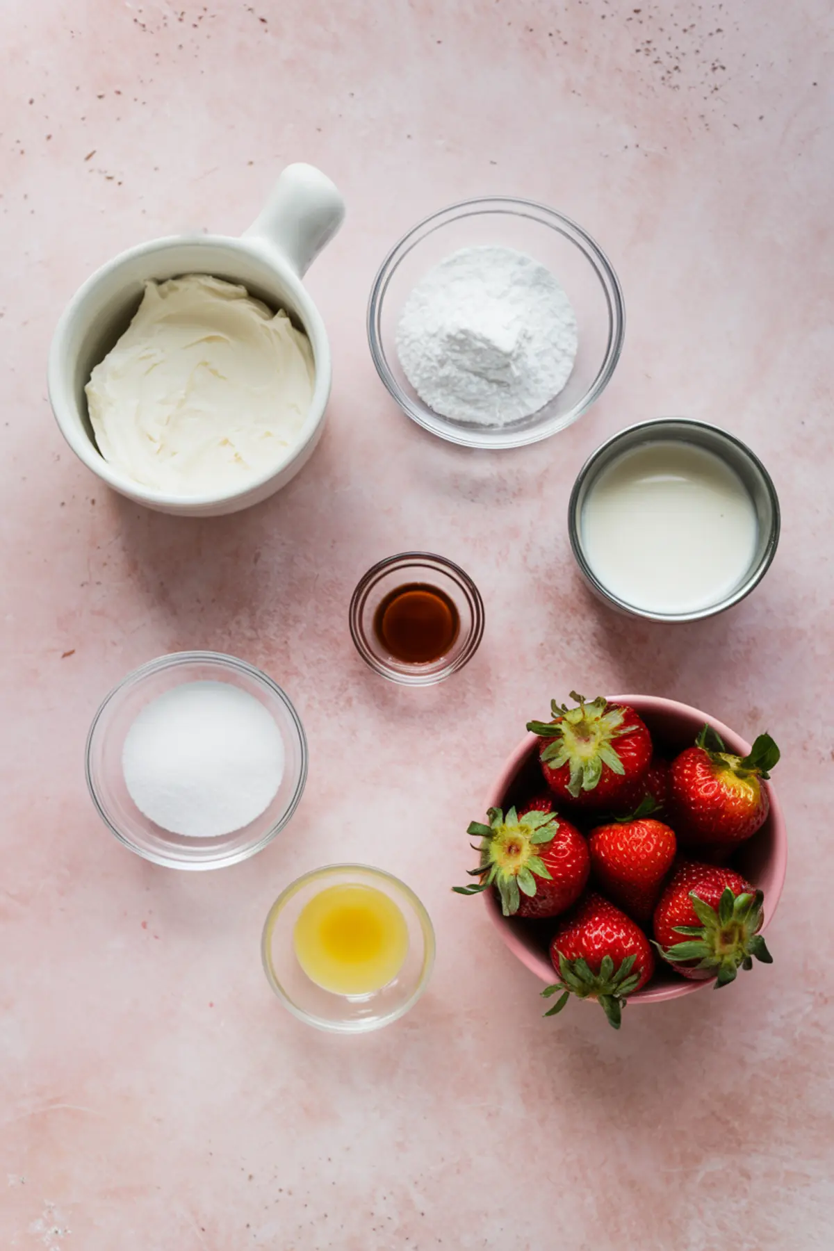 Flat lay of strawberry cheesecake dip ingredients including cream cheese, powdered sugar, heavy cream, fresh strawberries, granulated sugar, vanilla extract, and lemon juice on a pink background.