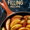 Close-up of a red-handled skillet filled with raw apple slices simmering in spiced brown syrup, topped with cinnamon sticks and dusted with ground cinnamon, beneath bold text reading “Apple Pie Filling Recipe” on a marble background.
