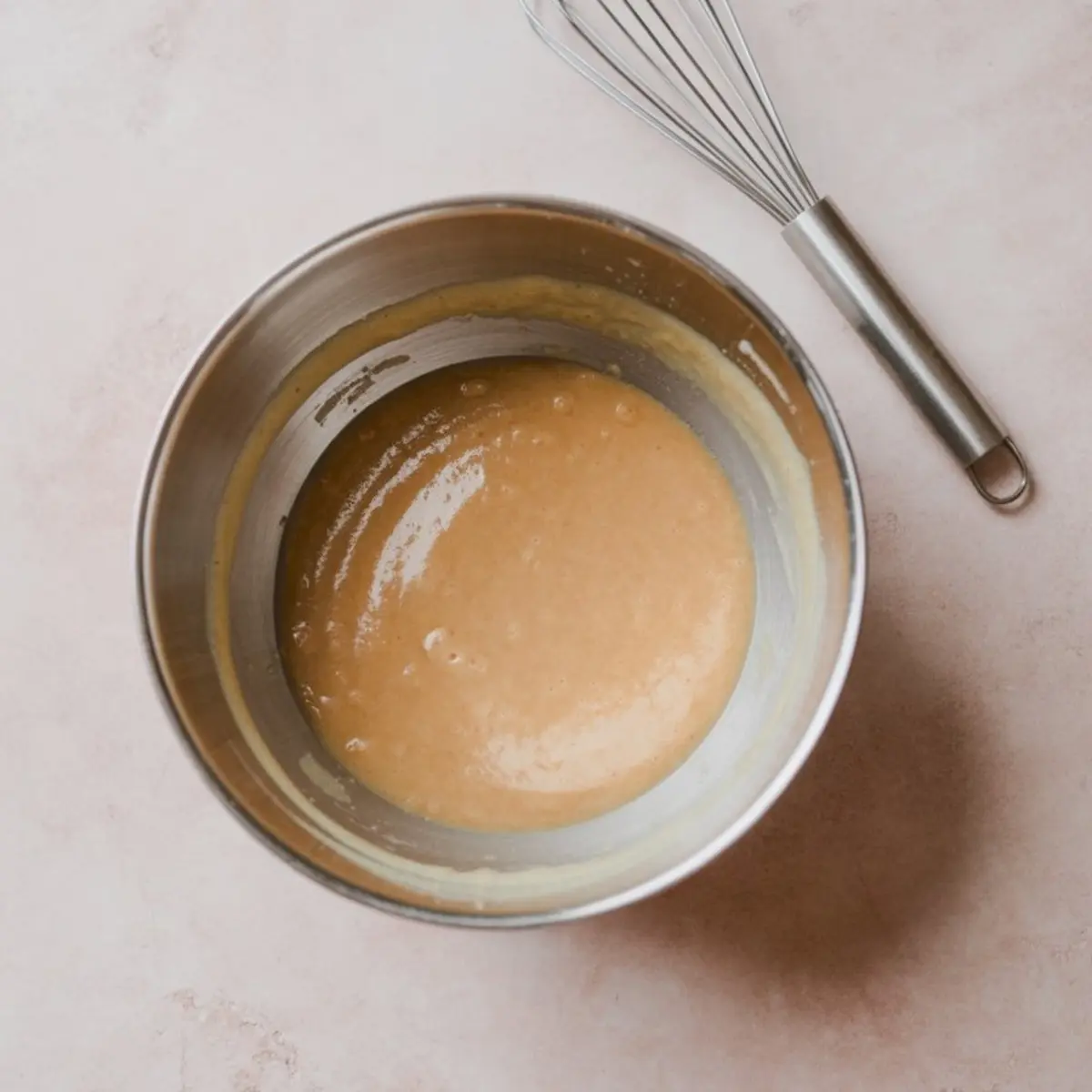 Mixing bowl filled with smooth butterscotch pie filling batter, sitting on a neutral countertop with a metal whisk nearby.