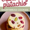 Top-down view of a stack of round cranberry pistachio shortbread cookies on a pink ceramic plate with visible chunks of cranberries and pistachios; includes recipe title in bold font.