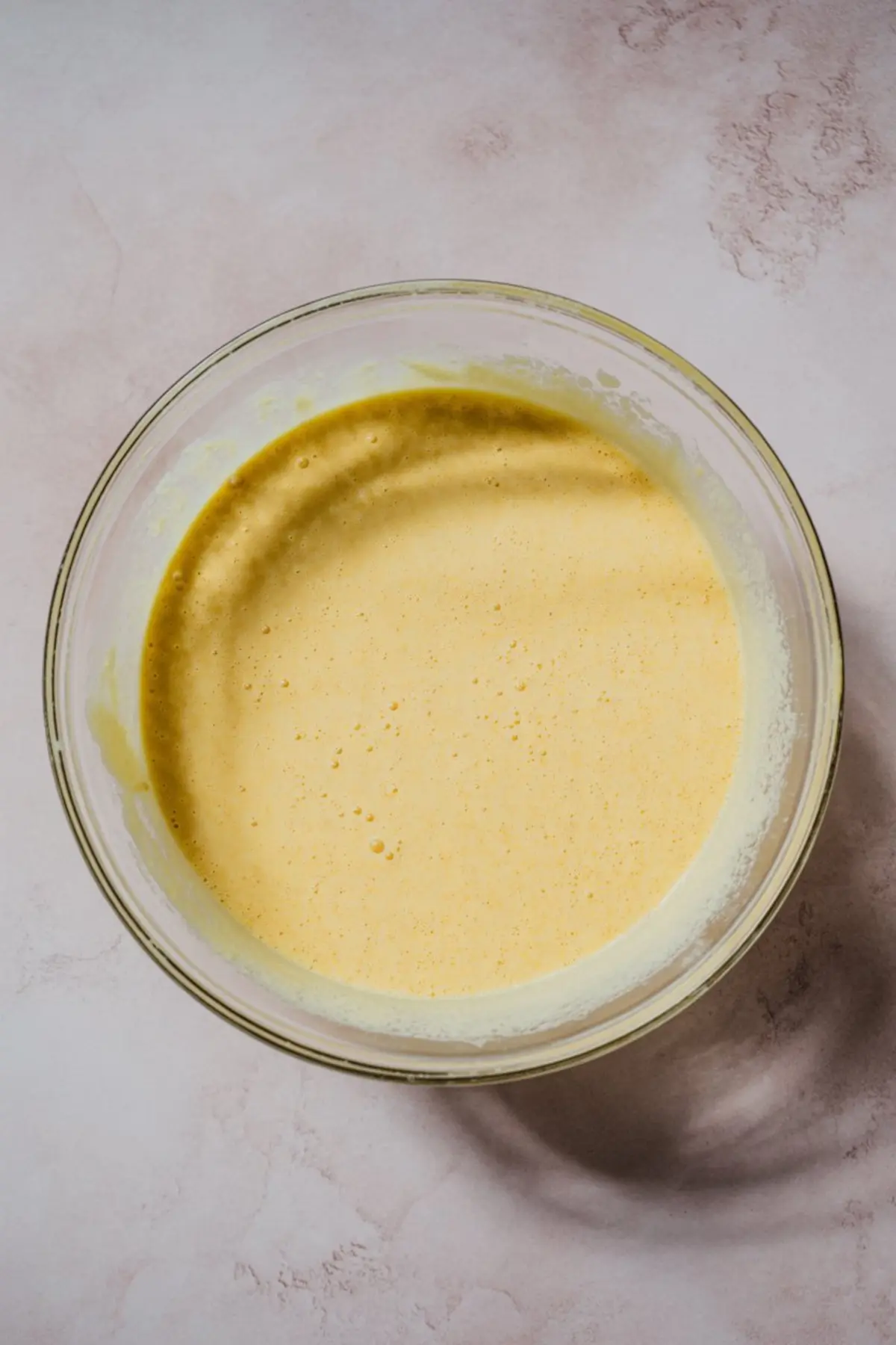 Smooth yellow custard mixture in a clear glass mixing bowl, showcasing the creamy egg-based filling for a classic homemade custard pie recipe.
