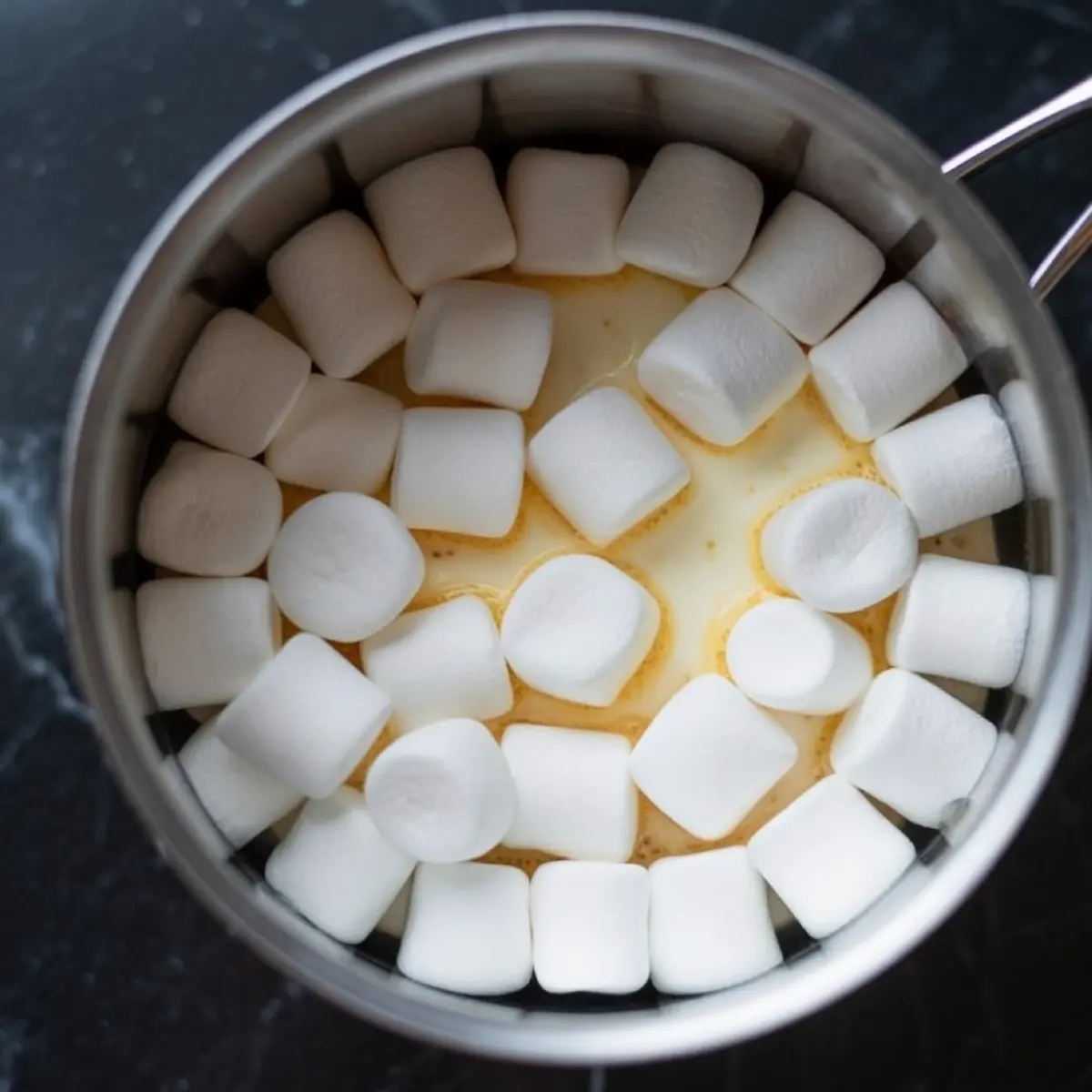Saucepan filled with mini marshmallows melting into cream and butter, ready for grasshopper pie filling.
