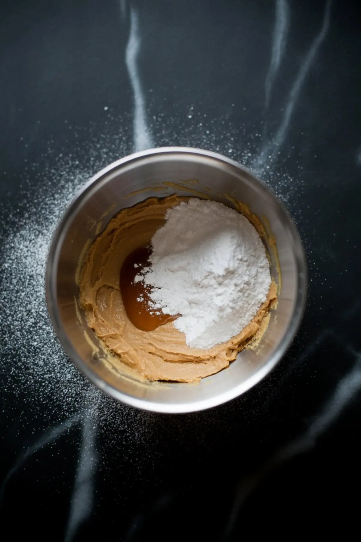 Mixing bowl filled with peanut butter mixture, powdered sugar, and brown sugar on a dark marble counter dusted with sugar.