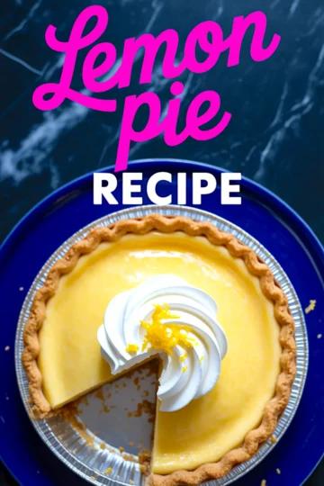 Overhead view of a whole lemon pie with whipped topping and lemon zest, placed in a foil pie dish on a dark marble surface with one slice removed.