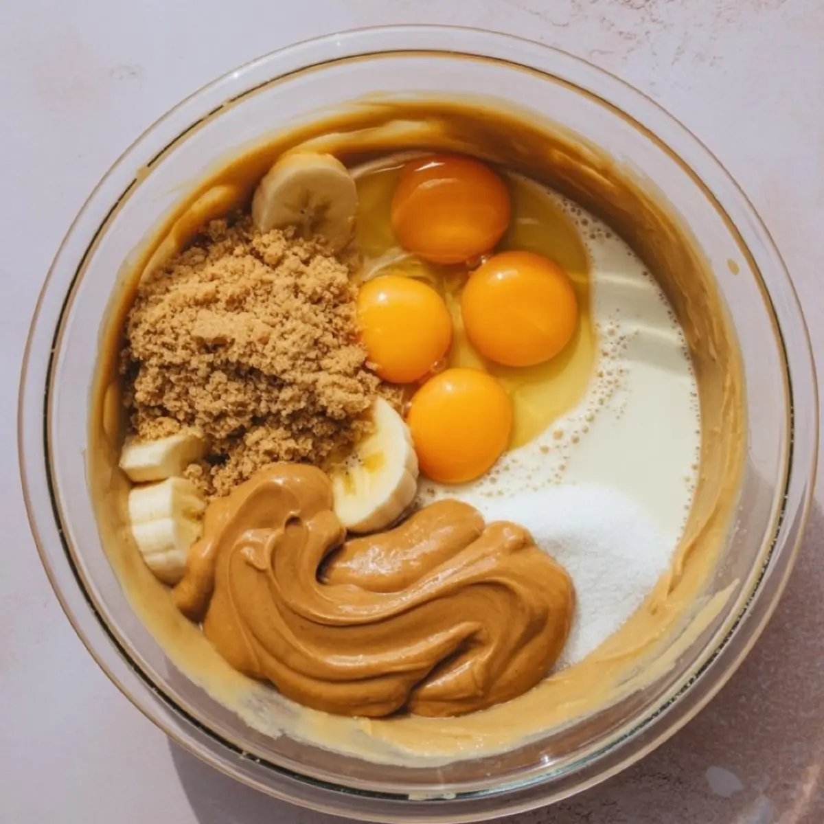 Raw banana bread batter in mixing bowl with eggs, peanut butter, milk, bananas, brown sugar - wet ingredients for healthy banana bread recipe