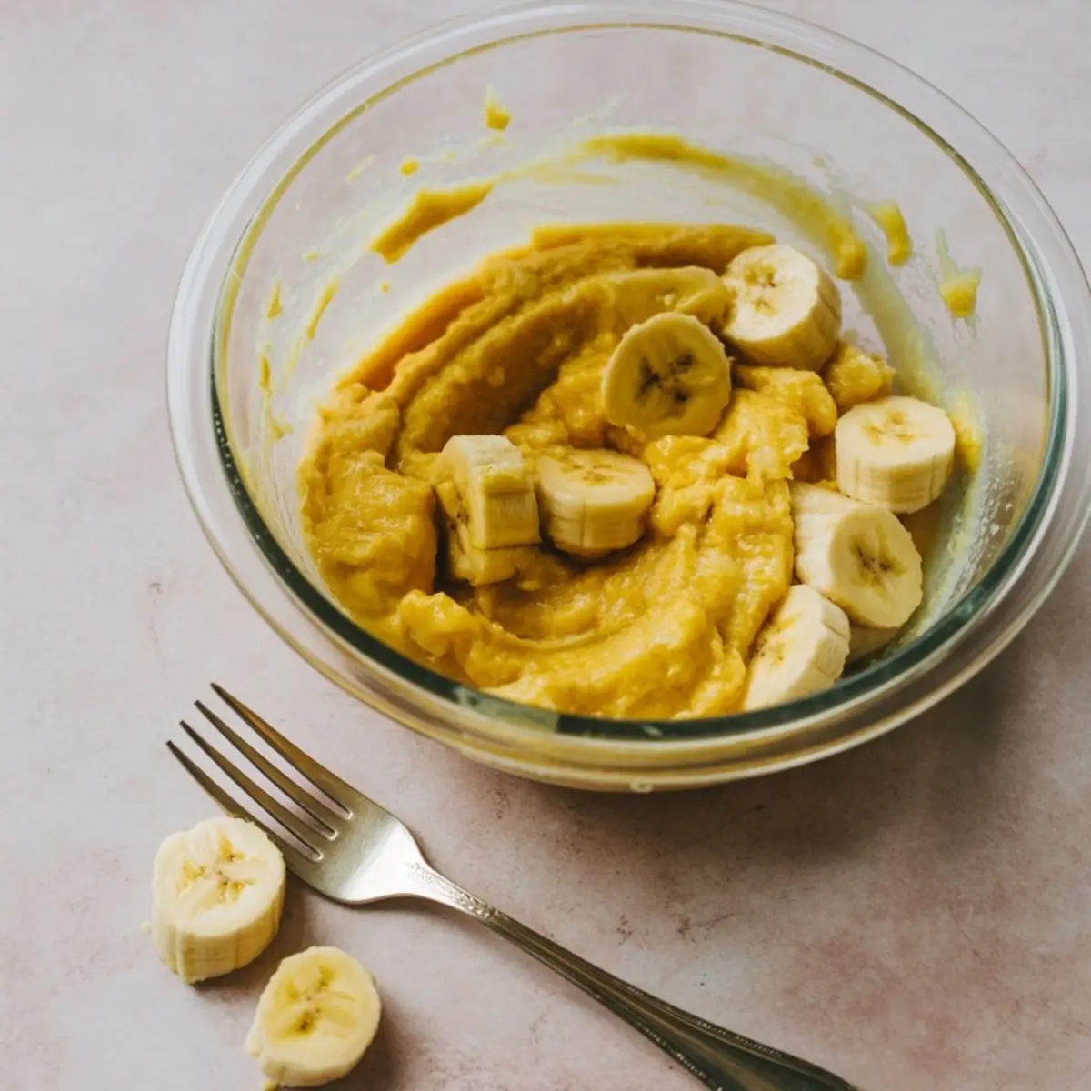 Mashed bananas and peanut butter mixture in glass bowl with fork - ingredients for healthy banana bread recipe using overripe bananas