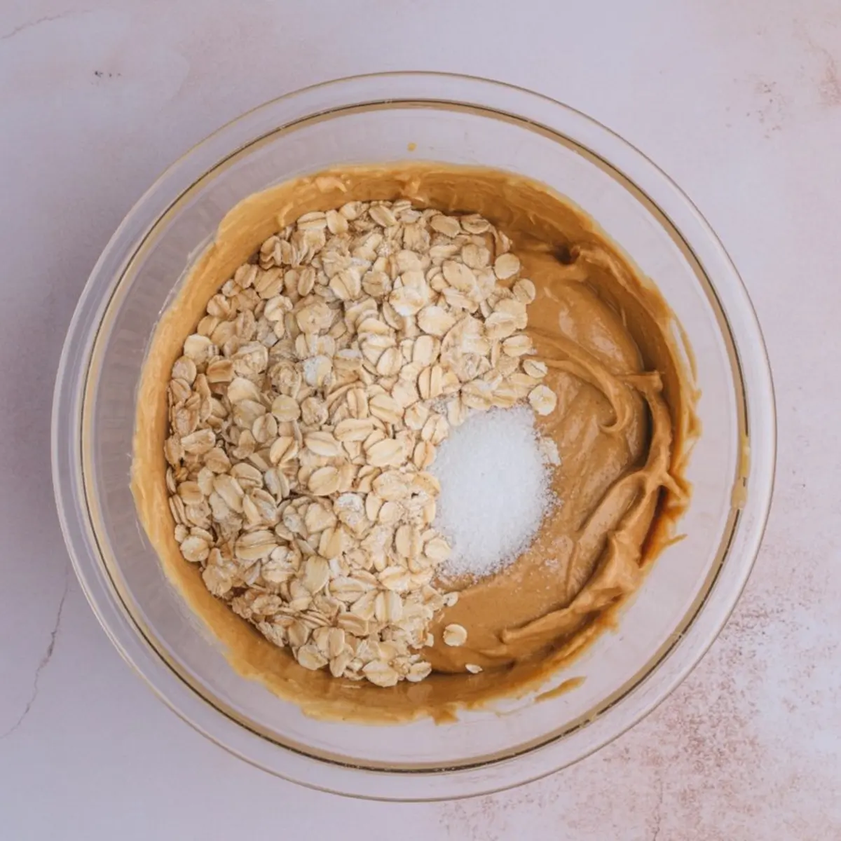 Top view of a mixing bowl showing peanut butter, oats, and granulated sugar just before blending for energy bites.